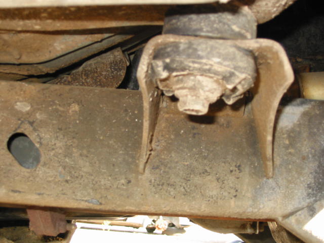 Underside of rusty vehicle frame with body mount and visible crack in the metal