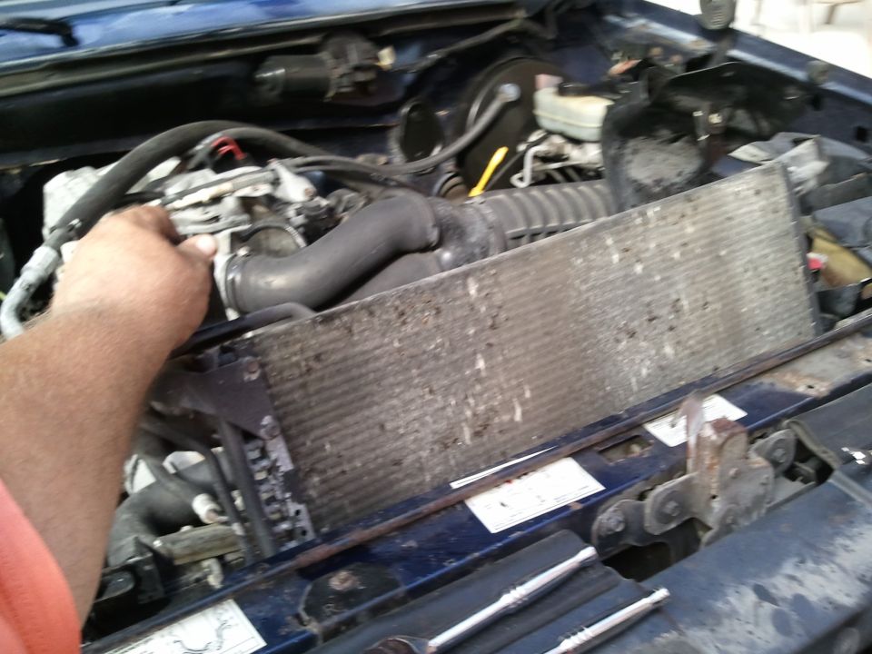 Blue vehicle engine bay with a dirty radiator and hoses, a hand is visible near the top