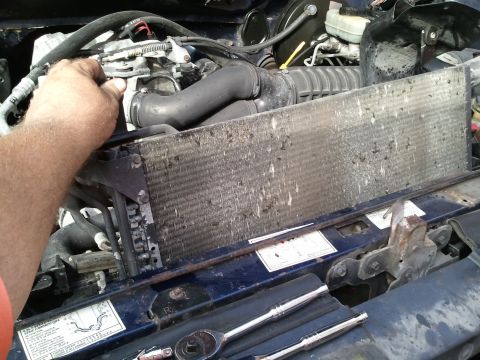1994 Ford Bronco - Mechanic works on a dirty radiator in the engine bay of a 1994 Ford Bronco.