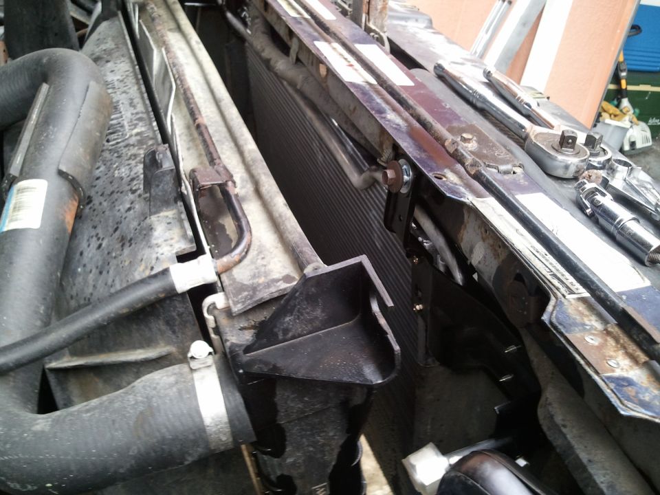 Close-up of vehicle radiator and AC condenser with hoses and mounting brackets. Tools are visible on top