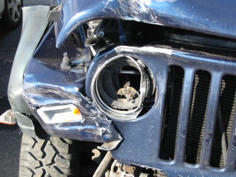 2002 Jeep Wrangler - Front view of a heavily damaged blue 2002 Jeep Wrangler, showing a broken headlight and dented grille.