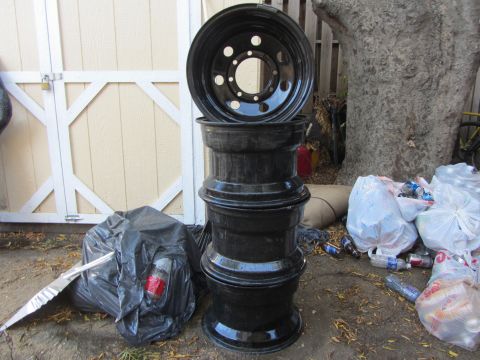 1987 Suzuki Samurai - Four black rims are stacked on the ground next to trash bags and a tree.