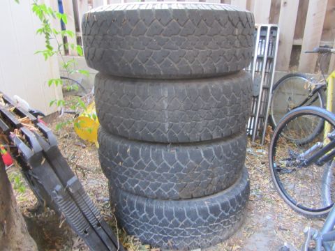 1987 Suzuki Samurai - A stack of four used tires sits on the ground next to a fence, with bicycles and other items in the background.