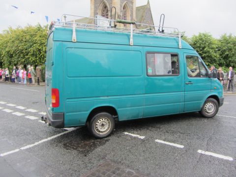 1968 Ford Mustang - A teal van with a roof rack is parked on a street with a church in the background.