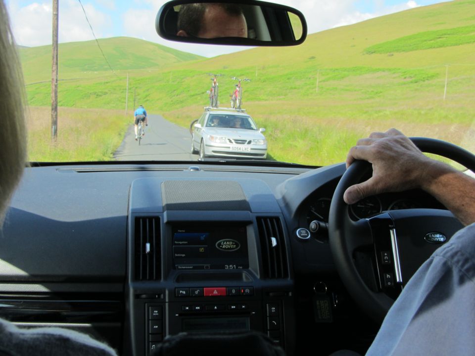 Silver car with bicycles on roof rack driving on a rural road