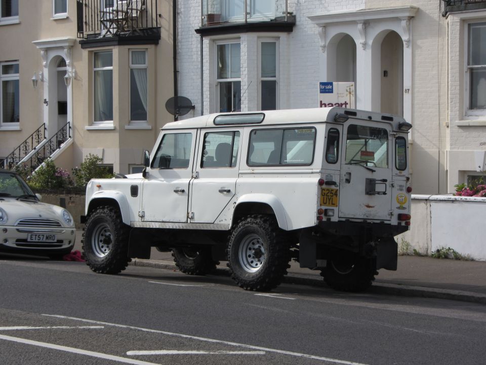 White Land Rover Defender 110 parked on street next to a Mini Cooper