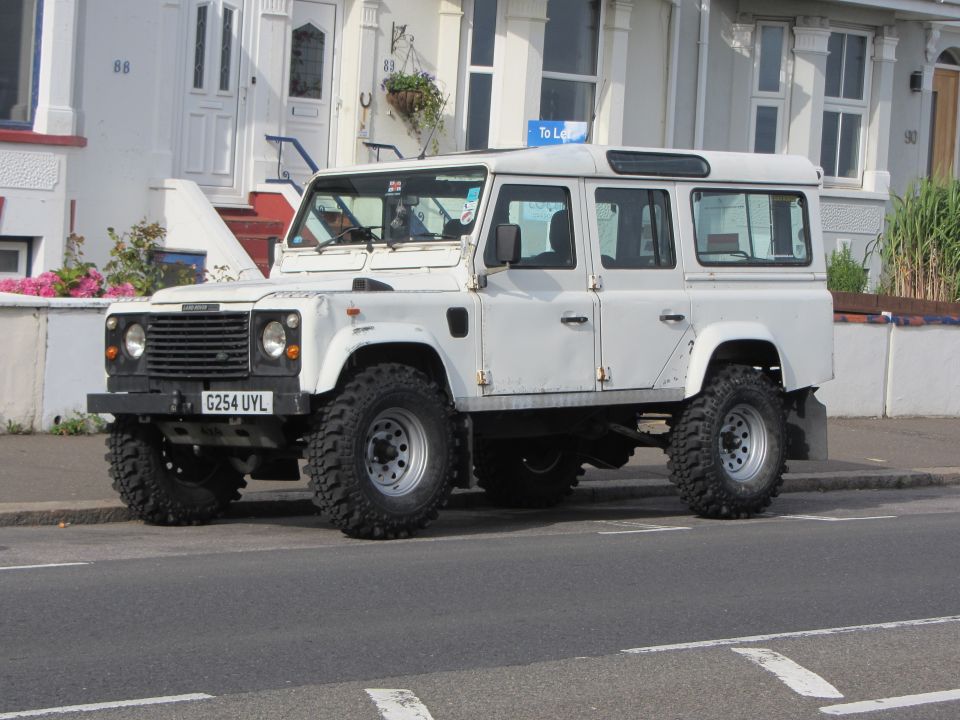 White Land Rover Defender 110 parked on street, front driver side visible, hood is up