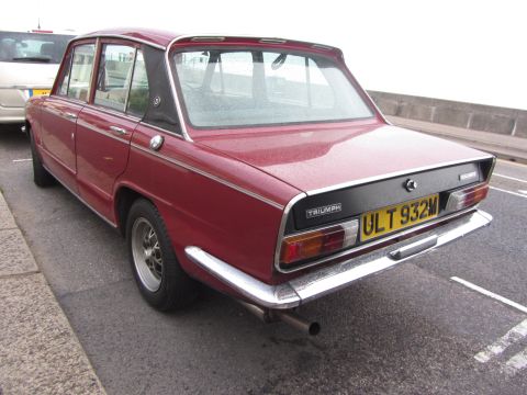 1968 Ford Mustang - The rear of a red Triumph Dolomite sedan is shown parked on a street, with a yellow license plate.