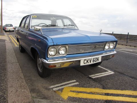 1968 Ford Mustang - A blue sedan with a chrome grille and dual headlights is parked on the side of a road.