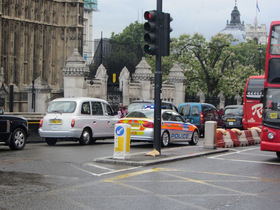 Silver police car with blue lights and orange stripes, next to a silver London taxi