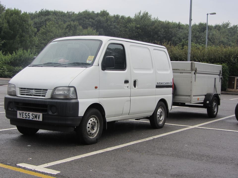 White Suzuki Carry van towing a silver cargo trailer in a parking lot