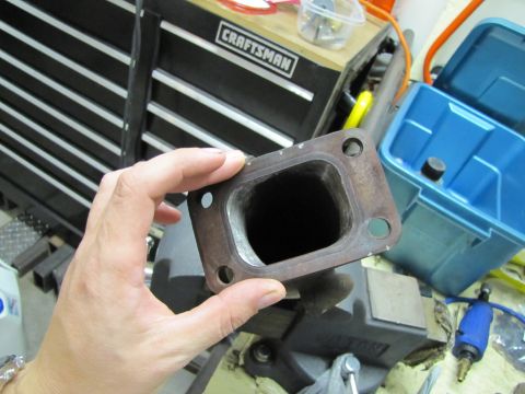 1993 Ford F-250 - A close-up shows a metal exhaust manifold flange being held by a hand, with workshop tools in the background.
