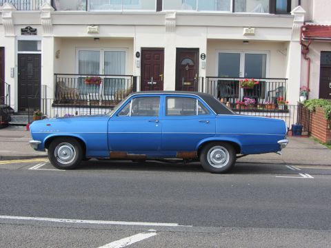 1968 Ford Mustang - A blue sedan is parked on the street in front of residential buildings.