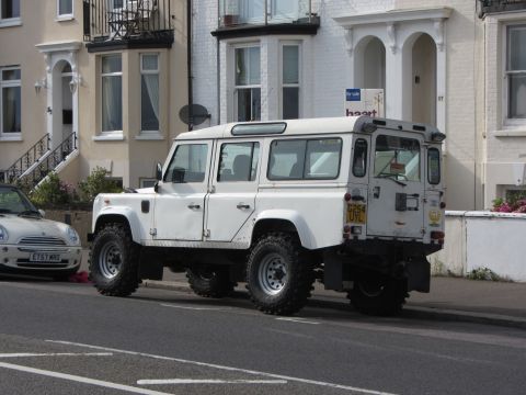 1968 Ford Mustang - White Land Rover Defender 110 parked on street with a Mini Cooper nearby.