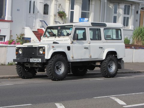 1968 Ford Mustang - A white Land Rover Defender 110 with off-road tires is parked on a residential street.