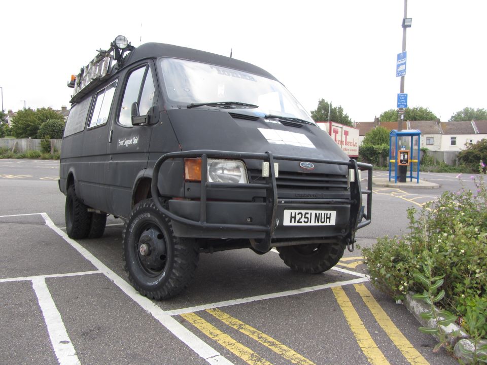 Black van with bull bar, roof rack, and off-road tires parked in a lot