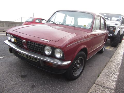 1968 Ford Mustang - Maroon Triumph Dolomite with a white Land Rover parked beside it on a street.