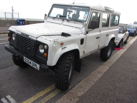 1968 Ford Mustang - A white Land Rover Defender is parked curbside next to other vehicles.