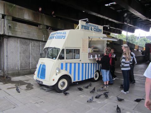 1968 Ford Mustang - A traditional fish and chips food truck is parked under a bridge, with customers lining up to order.