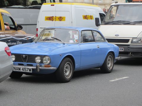 1968 Ford Mustang - A blue Alfa Romeo coupe is seen in traffic next to a white van.