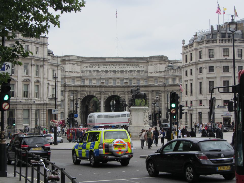 London street with a police SUV and other cars near a large archway