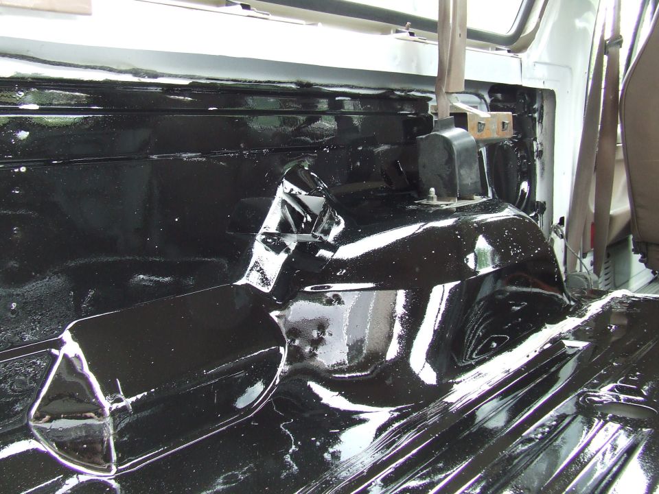 Interior floor of a vehicle coated in black, showing the transmission tunnel and seatbelt anchors