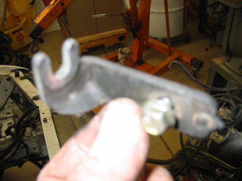 1993 Ford Taurus - A hand holds up a stamped-steel bracket with a forked/hooked end and a zinc-plated nut and stud through one of its mounting holes, photogra…