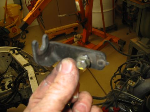 1993 Ford Taurus - A hand holds up a flat steel bracket with a forked hook end and a bolt-and-nut through a slotted mounting boss, likely a clutch or shift le…