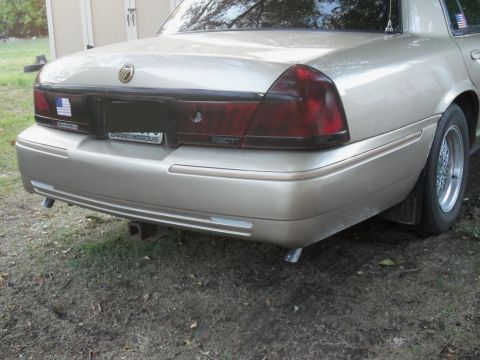 2000 Mercury Grand Marquis - Rear view of a gold 2000 Mercury Grand Marquis, showing its distinctive taillights and a trailer hitch.