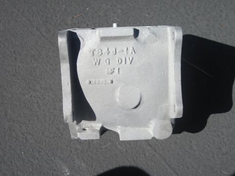 1979 Ford Bronco - A single gray metal casting part is shown against a dark surface, with text stamped on its side.