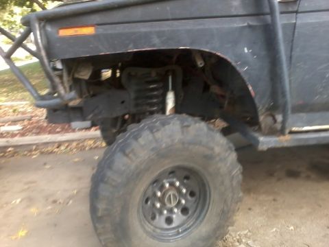 1986 Ford Bronco - Close-up of a modified black SUV's front wheel well and fender, showing off-road suspension components.