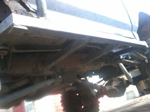 1986 Ford Bronco - The undercarriage of a vehicle reveals its suspension and frame, with visible signs of wear and modification.