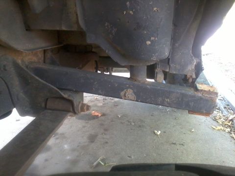 1986 Ford Bronco - Close-up view of the rusted undercarriage of a vehicle, with visible suspension parts and frame damage.
