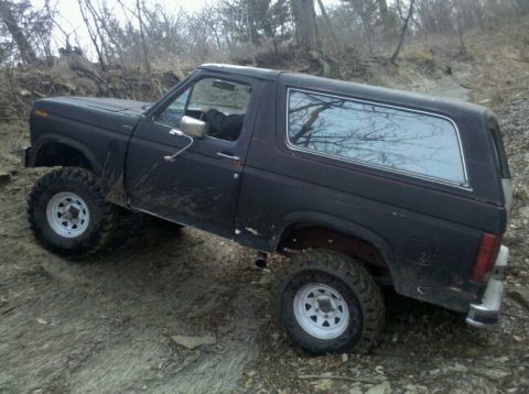 1986 Ford Bronco - This black Ford Bronco is seen off-road, showing its side profile and chrome window trim.