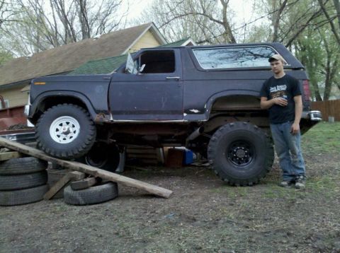1986 Ford Bronco - A man stands beside a lifted Ford Bronco, which appears to be undergoing some modifications or repairs.
