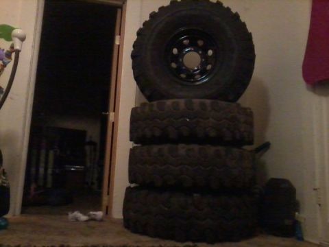 1986 Ford Bronco - A stack of four off-road tires is visible indoors, with a doorway and a hint of a room in the background.
