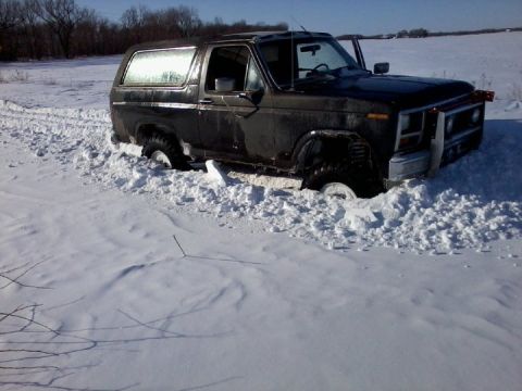 1986 Ford Bronco - Ford Bronco stuck in a snowy field, tires buried in snow drifts.