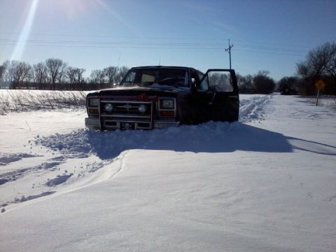 1986 Ford Bronco - A dark-colored Ford Bronco is stuck in deep snow on a rural road.