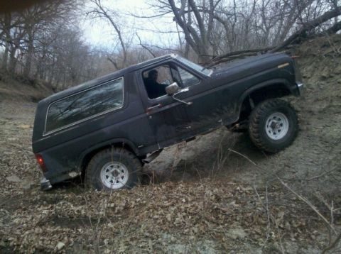 1986 Ford Bronco - Black SUV navigating an off-road incline with trees in the background.