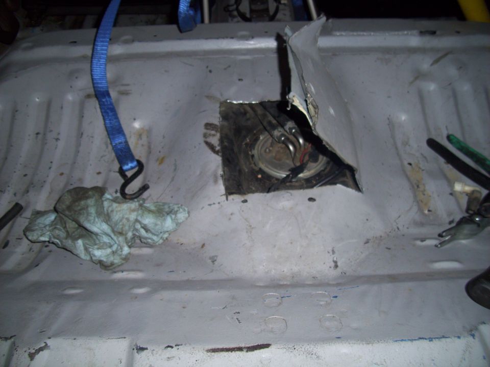 cutout in car floor showing fuel pump assembly, with straps and rags nearby