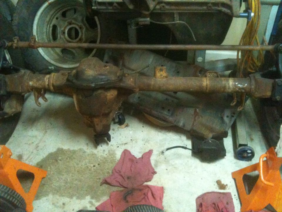 Rusted front axle assembly with steering linkage, supported by orange jack stands