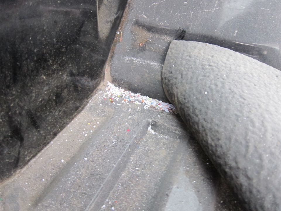 Close-up of a truck bed liner showing dirt and small colorful debris accumulated in a corner