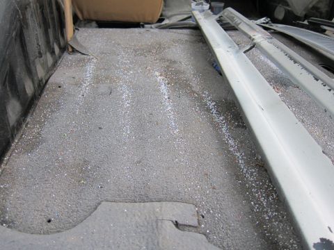 1987 Dodge 1500 - The interior of a vehicle's cargo area shows a textured floor with scattered debris and parts of seats.
