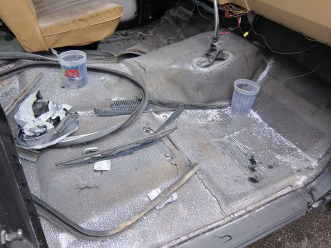 1987 Dodge 1500 - The interior of a vehicle shows a messy floor with debris and white powder, along with tan seats and exposed wiring.