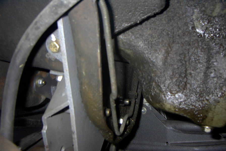 Underbody shot of a 1994 Ford Bronco showing greasy oil pan area, metal bracket, and linkage hardware