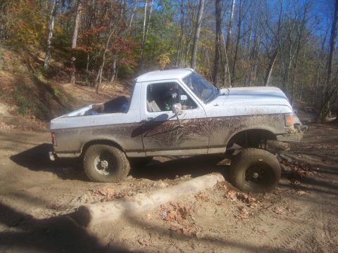 1989 Ford Bronco - A white 1987 Ford Bronco navigates a muddy off-road course with fallen leaves on the ground.