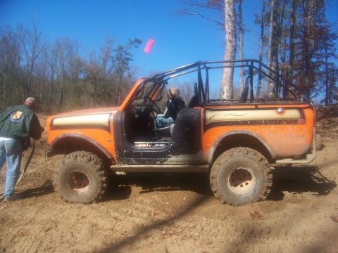 1989 Ford Bronco - An off-road vehicle is parked on a dirt trail surrounded by trees under a clear blue sky.