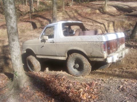 1989 Ford Bronco - A white Ford Bronco navigates a muddy off-road trail, its tires covered in dirt.