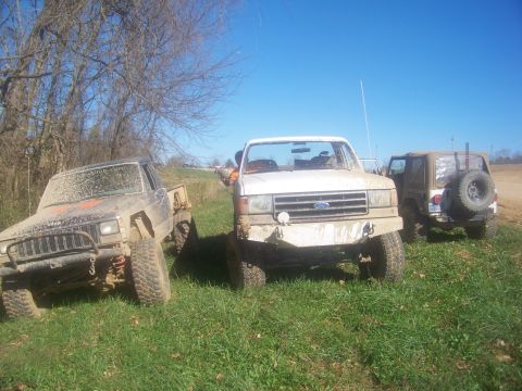 1989 Ford Bronco - Three off-road vehicles are parked on a grassy field on a sunny day.