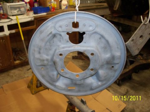 1990 Ford Bronco - A gray brake drum backing plate is suspended by a wire, ready for installation or refinishing.